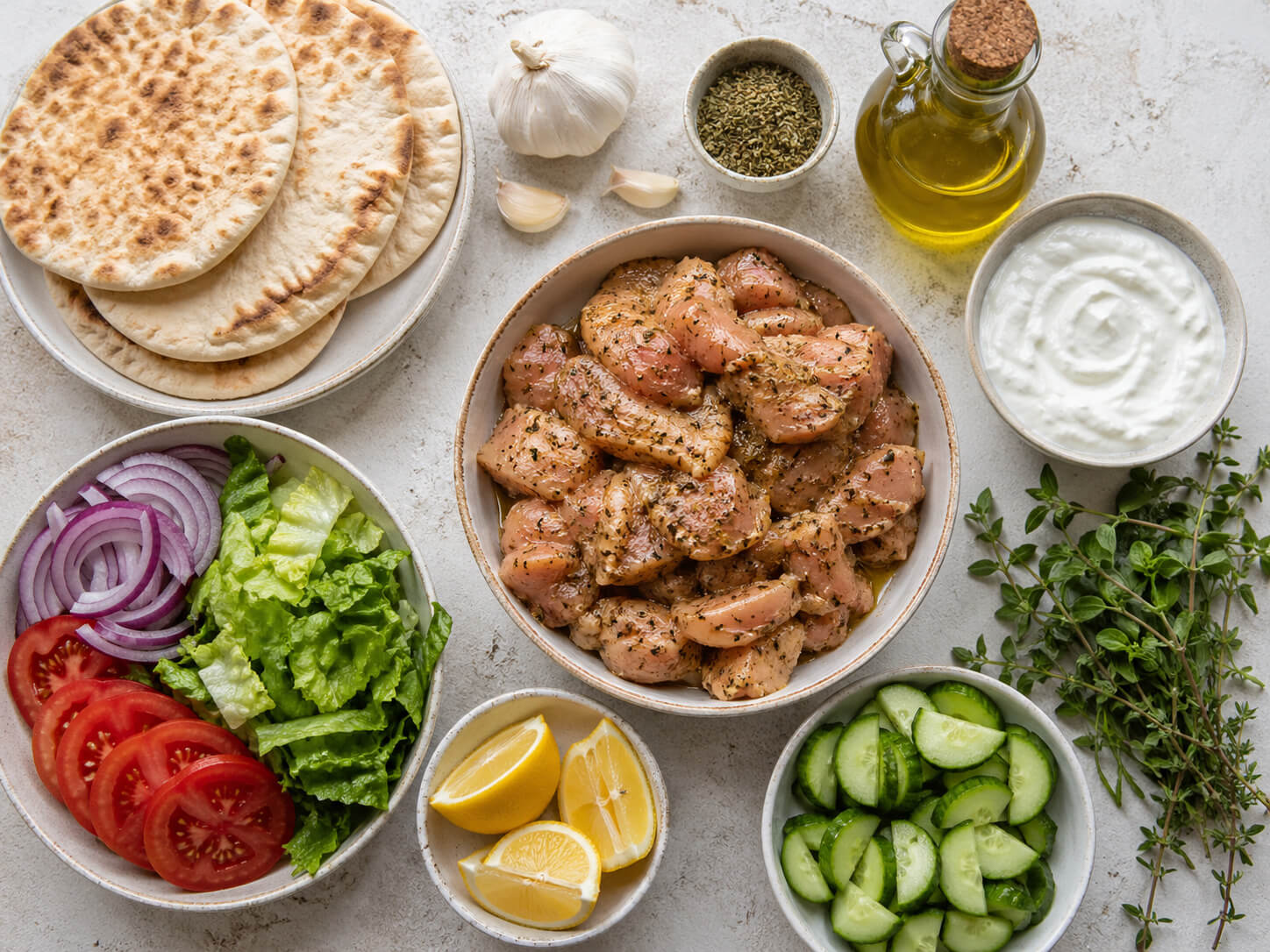 Chicken gyro ingredients with pita bread, tomatoes, onions, lettuce, cucumber, yogurt, garlic, herbs, and olive oil