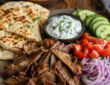 Easy gyro meat recipe with sliced homemade gyro meat, warm pita, vegetables, and tzatziki sauce