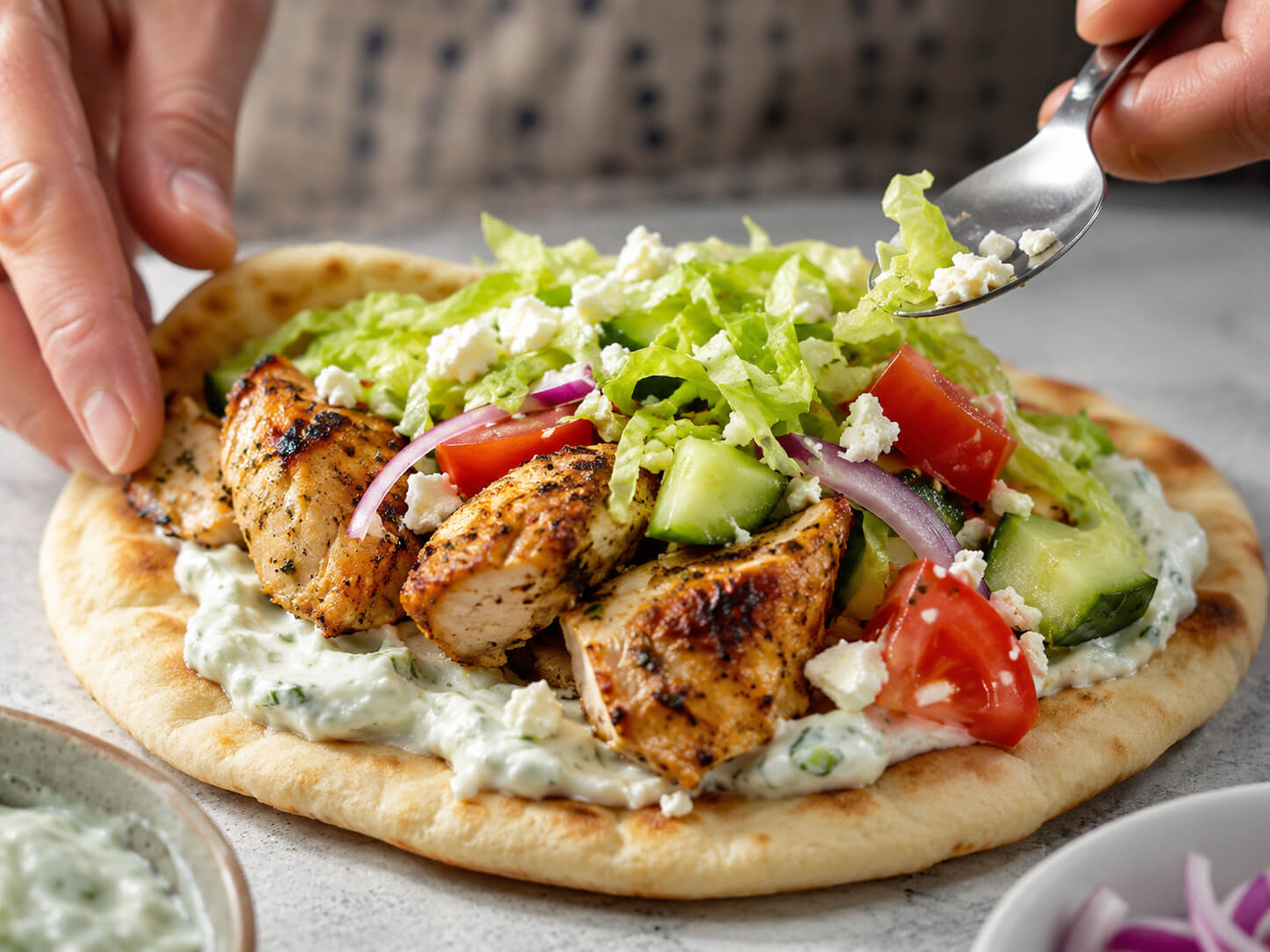 Chicken souvlaki pita being assembled with grilled chicken, vegetables, and tzatziki sauce