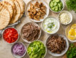 Gyro wrap ingredients with pita bread, grilled chicken, beef, lamb, cucumber, tomato, red onion, lettuce, feta, and tzatziki sauce