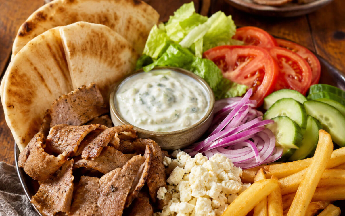 Gyro toppings with pita bread, sliced gyro meat, lettuce, tomato, cucumber, red onion, feta, fries, and tzatziki sauce