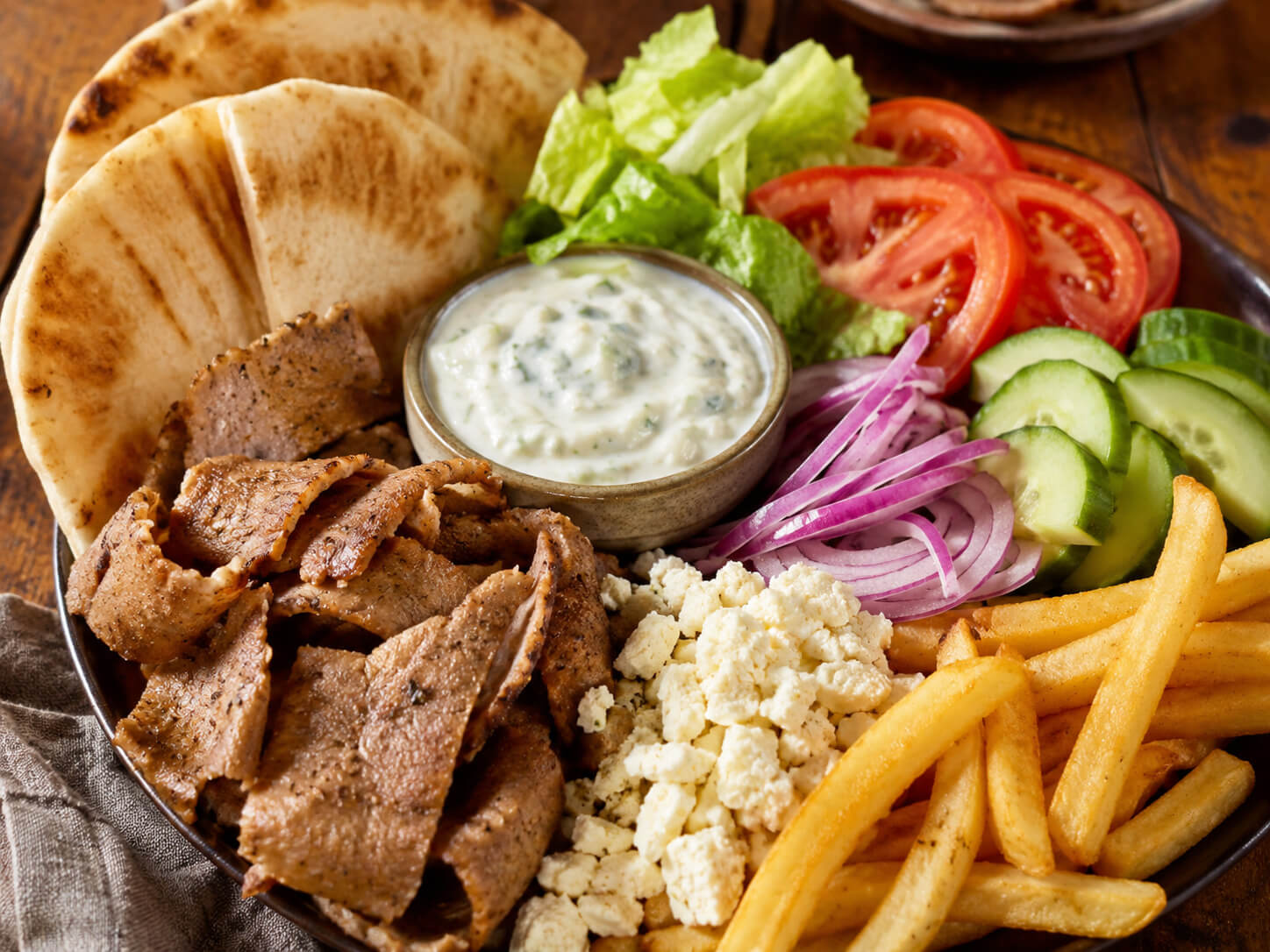 Gyro toppings with pita bread, sliced gyro meat, lettuce, tomato, cucumber, red onion, feta, fries, and tzatziki sauce