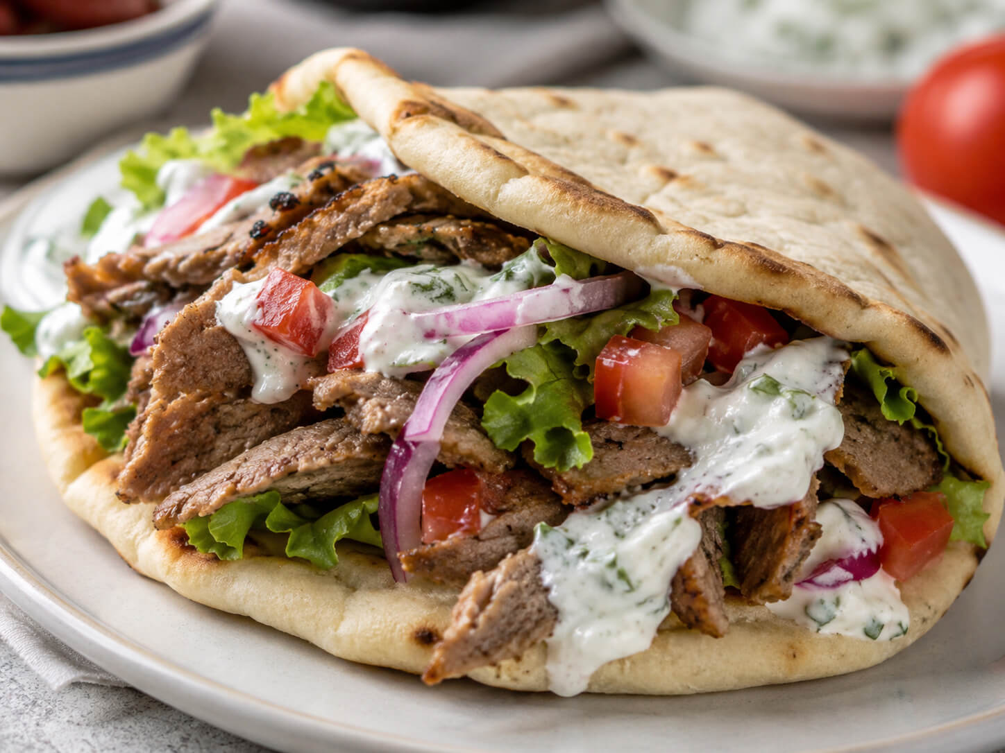 Pita for gyros with soft Greek flatbread, sliced gyro meat, tomatoes, onions, lettuce, and tzatziki sauce