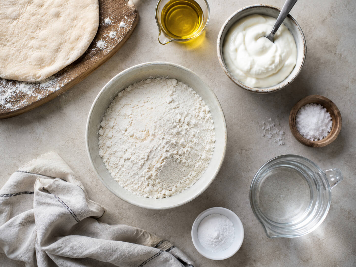 Greek flatbread ingredients with flour, Greek yogurt, olive oil, salt, baking powder, and warm water