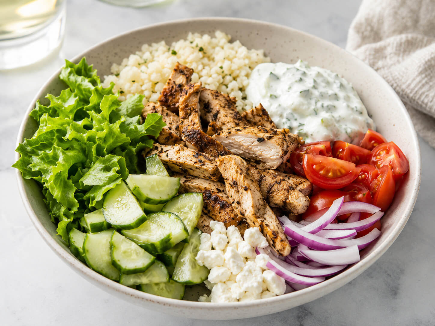 Gyro meal prep bowls with sliced Greek chicken, rice, cucumber, tomato, lettuce, red onion, feta, and tzatziki sauce