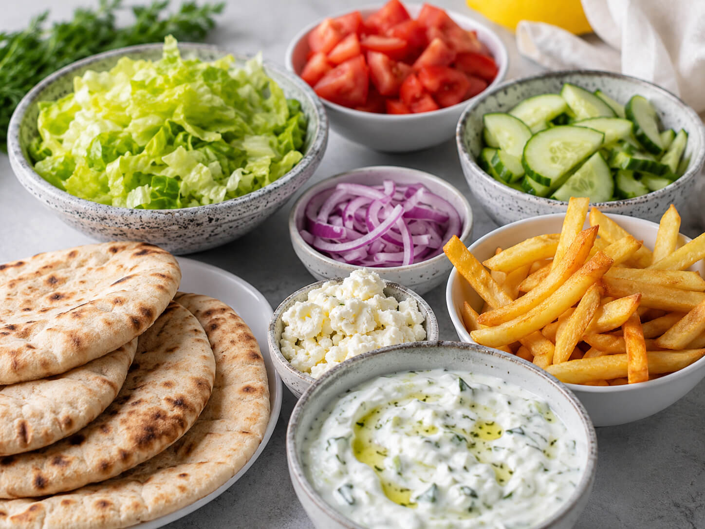 Gyro fillings with lettuce, tomato, cucumber, red onion, feta cheese, fries, pita bread, and tzatziki sauce