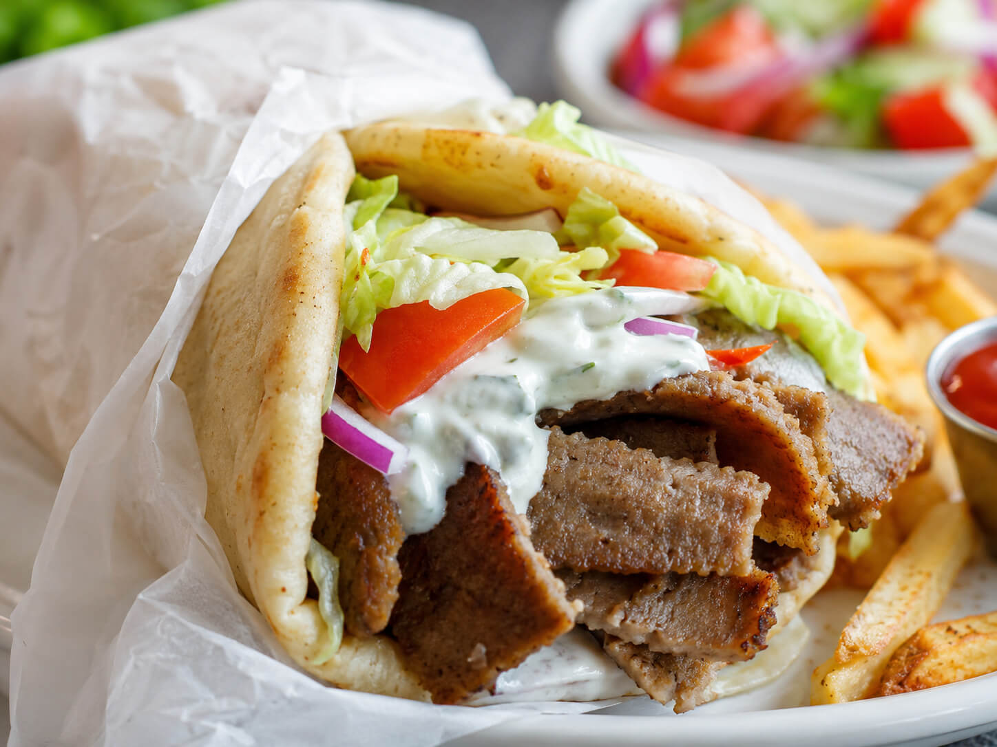 Restaurant-style gyro recipe with sliced gyro meat, warm pita, lettuce, tomato, onion, and creamy sauce