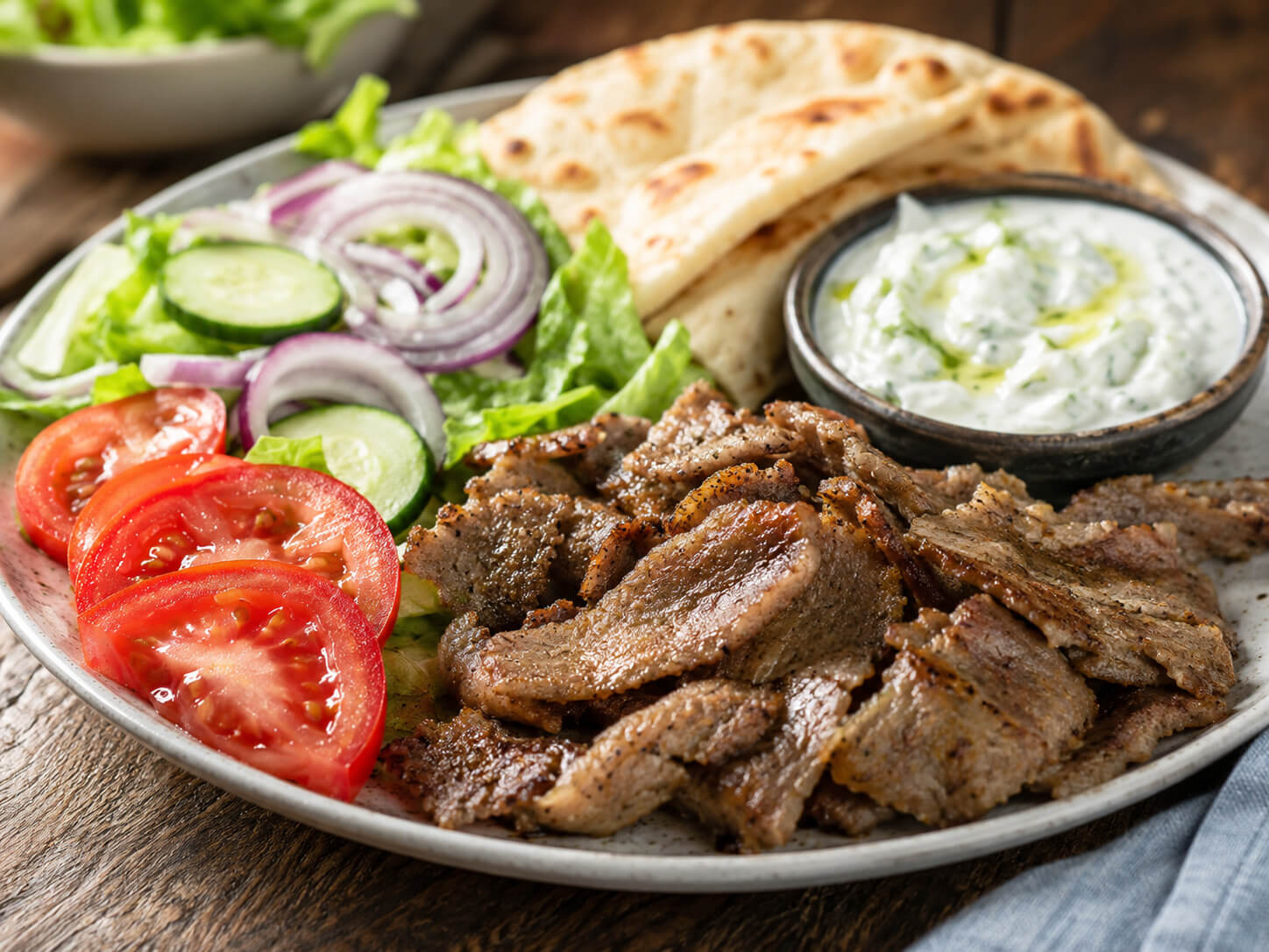 Homemade gyro recipe ingredients with ground meat, pita, tomatoes, cucumber, onion, herbs, and sauce